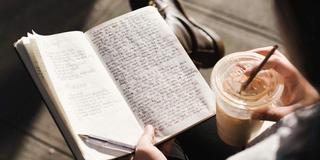 A person journaling with a cup of coffee.