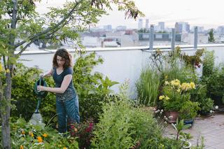 A woman tending to her urban rooftop garden with a city skyline in the background.